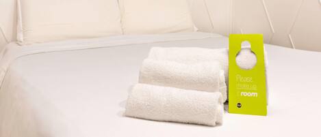 Una habitación de hotel con una cama bien hecha, ropa de cama blanca y un letrero verde en la pared.