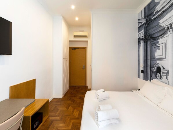 Habitación de hotel con cama, escritorio, silla, televisor y un pasillo que conduce a otra habitación.