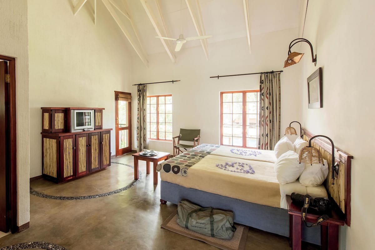 Habitación de hotel con cama, televisor, aparador de madera y baño visible a través de una puerta abierta.