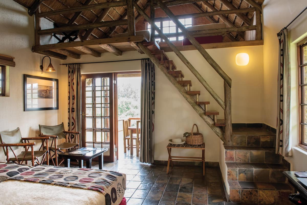 Una habitación con escalera de madera, cama, mesa y sillas.