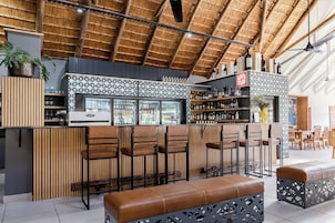 Una zona de bar con techo de paja, paredes de listones de madera y una variedad de botellas y vasos en estanterías.