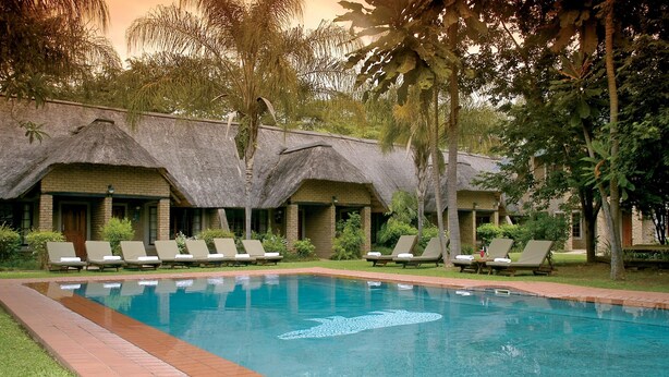 A swimming pool with lounge chairs and a thatched-roof building. - Hippo Hollow Country Estate (Mbombela)