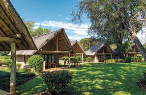 Een accommodatie in bungalowstijl met rieten daken, omgeven door verzorgde gazons en bomen.