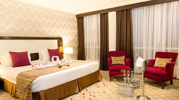 Habitación de hotel con una cama grande, dos sillones rojos, una mesa de centro de cristal y un minibar.