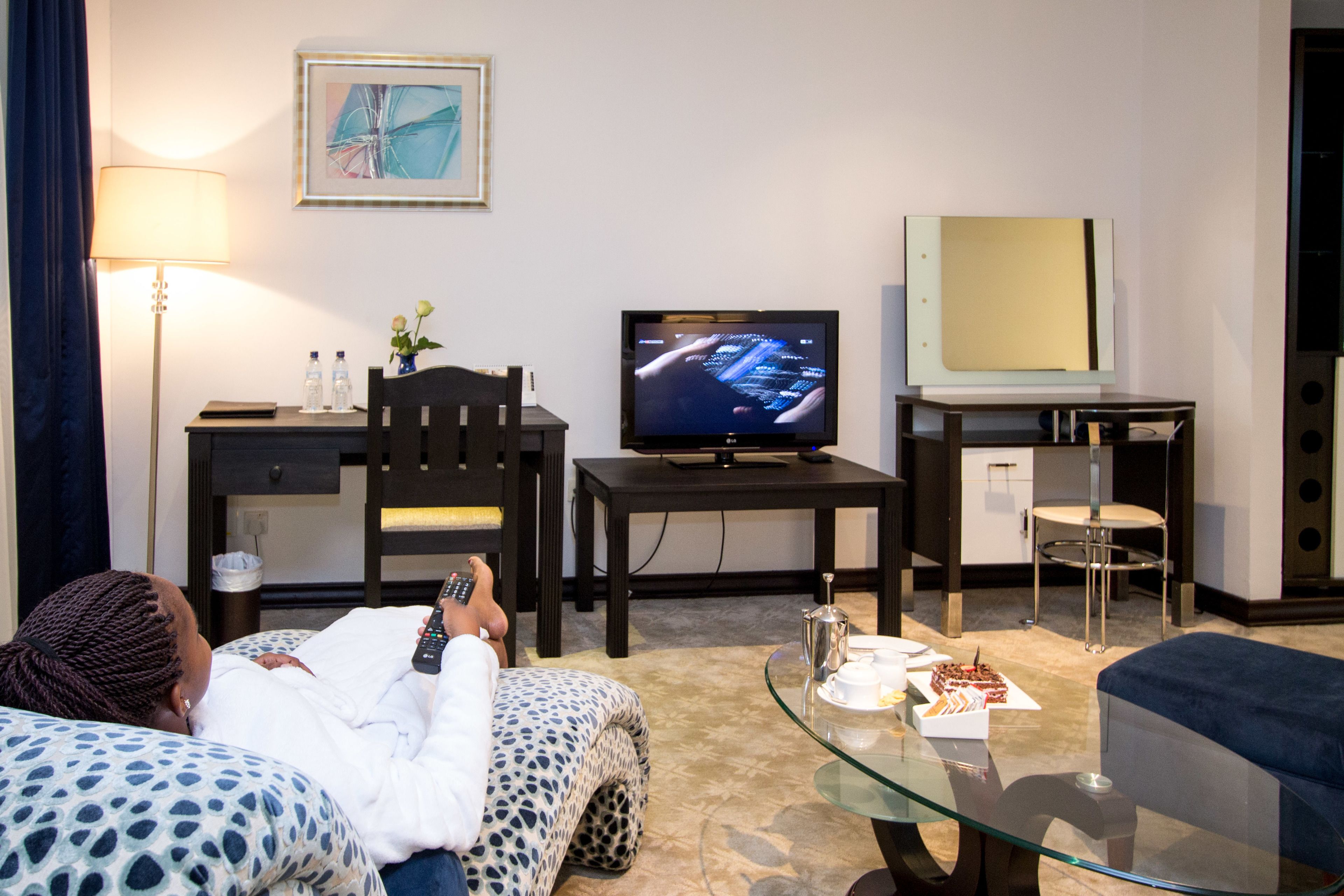 A hotel room with a bed, a TV, a desk with a chair, a glass coffee table, and a sofa.
