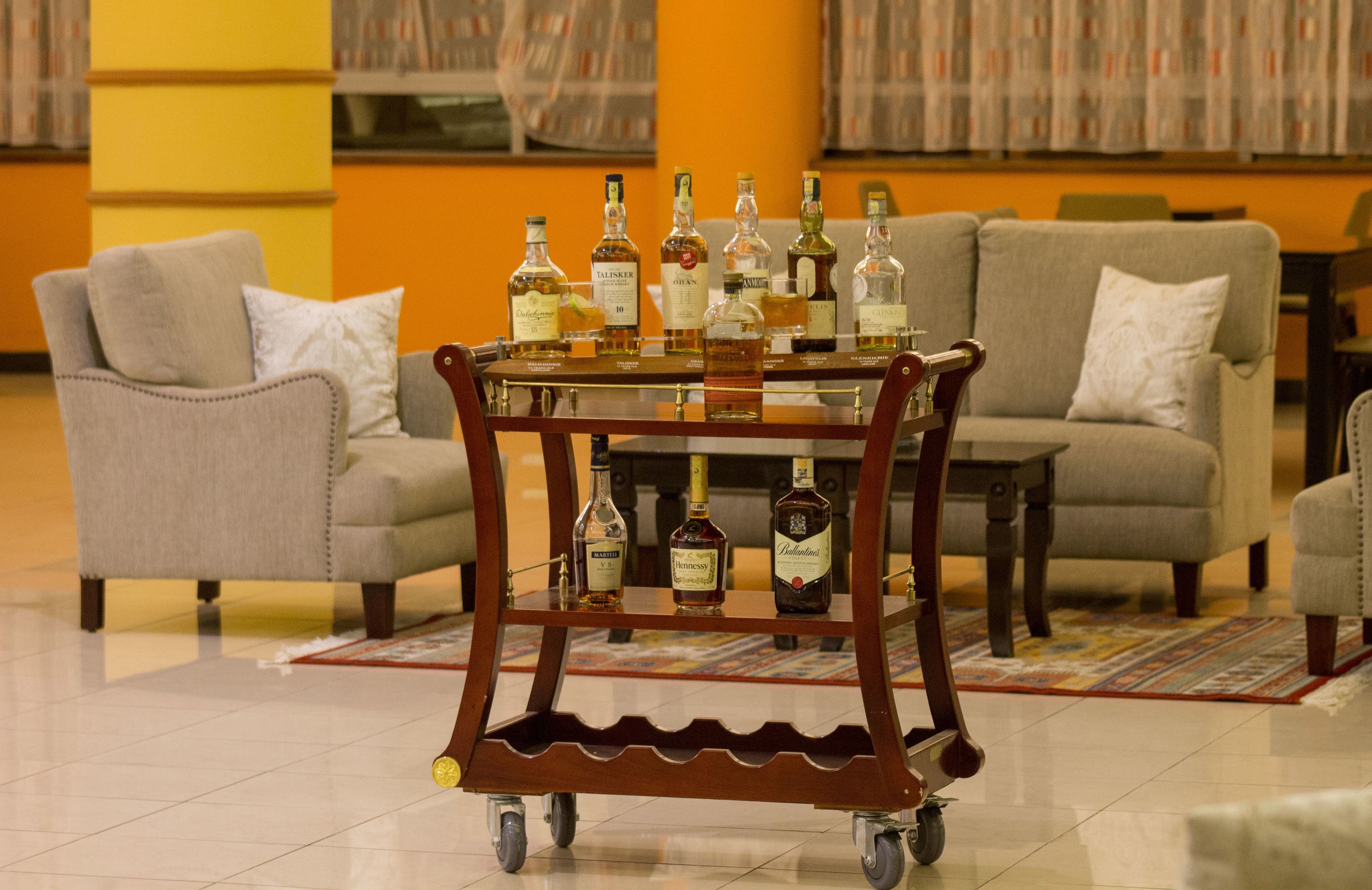 Un carrito con varias botellas de licores en una habitación con dos sofás y una alfombra estampada.