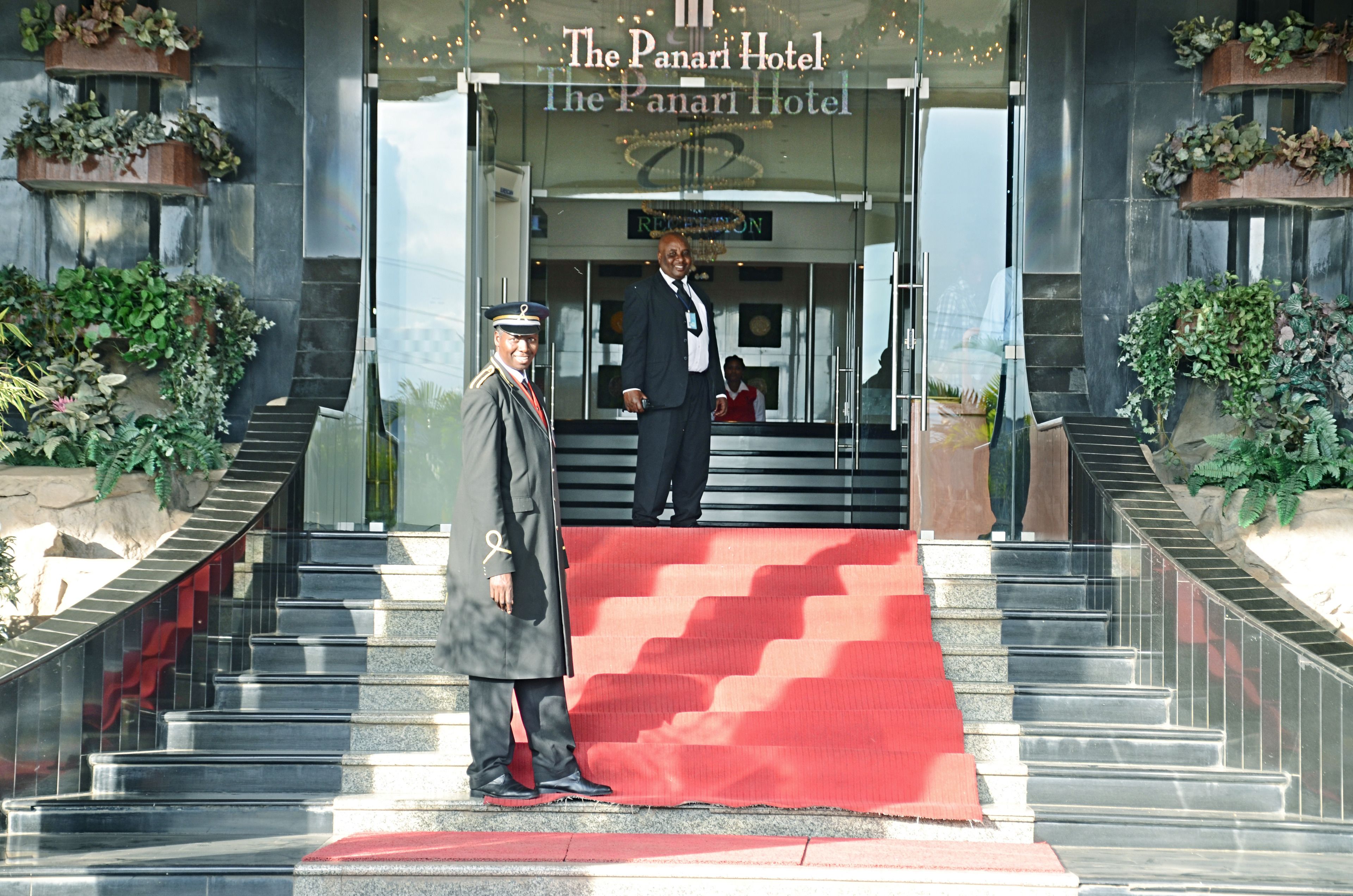 L’entrée d’un hôtel, avec un tapis rouge, un escalier et une enseigne indiquant « The Panari Hotel ».