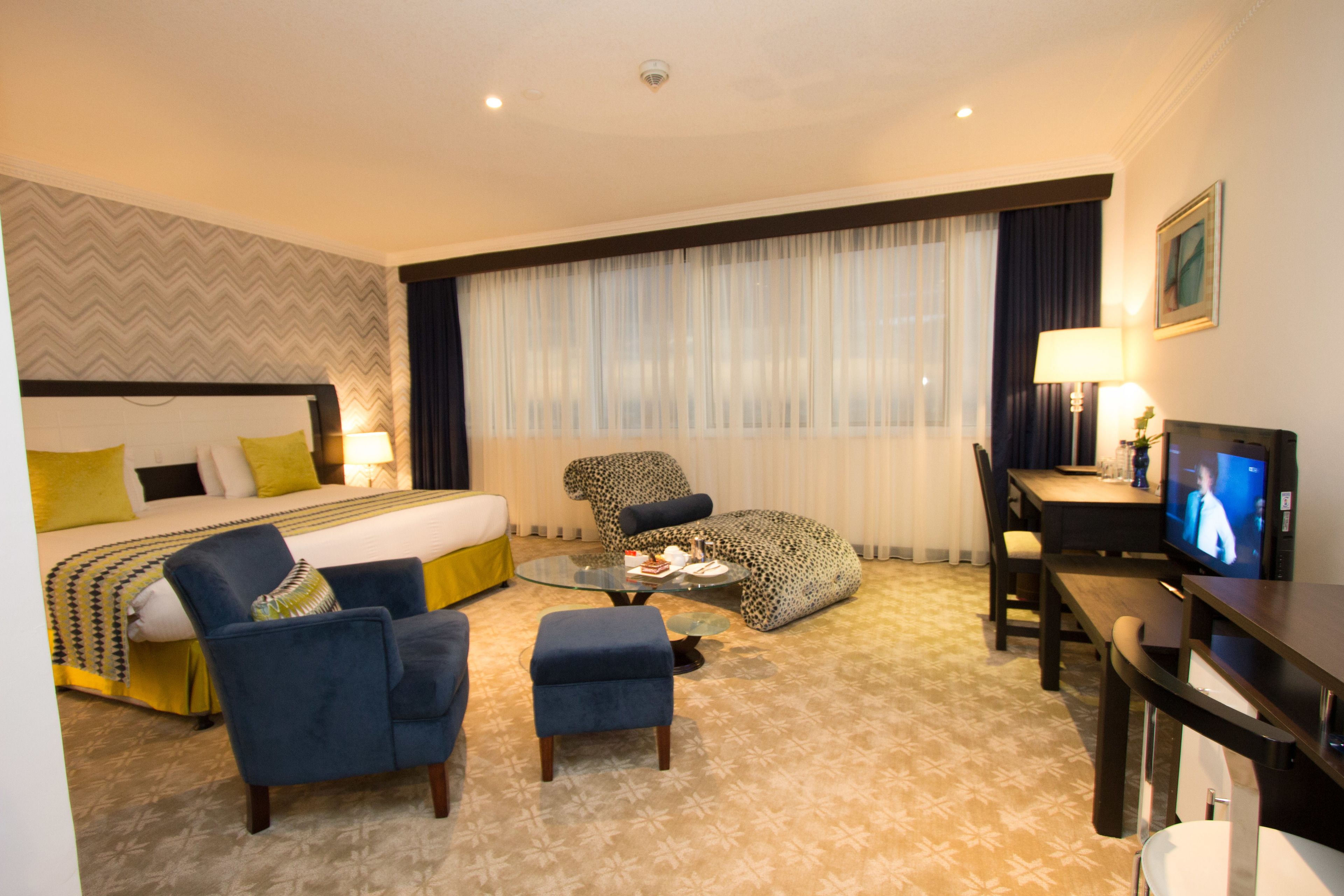 A hotel room with a bed, a desk with a television, a chair, a sofa, and a coffee table.