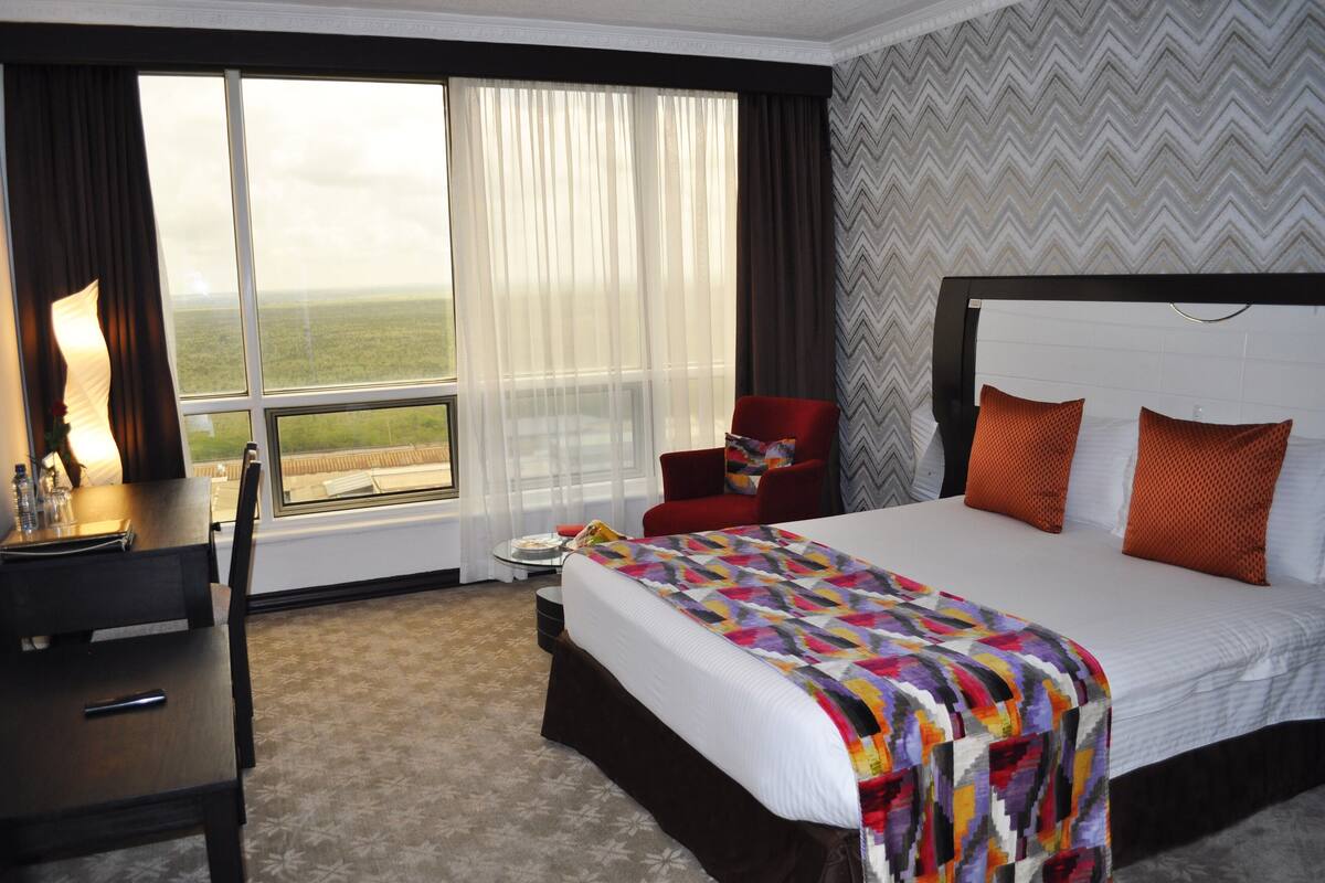 A hotel room with a large bed, a desk, a chair, and a view of the outdoors through the window.