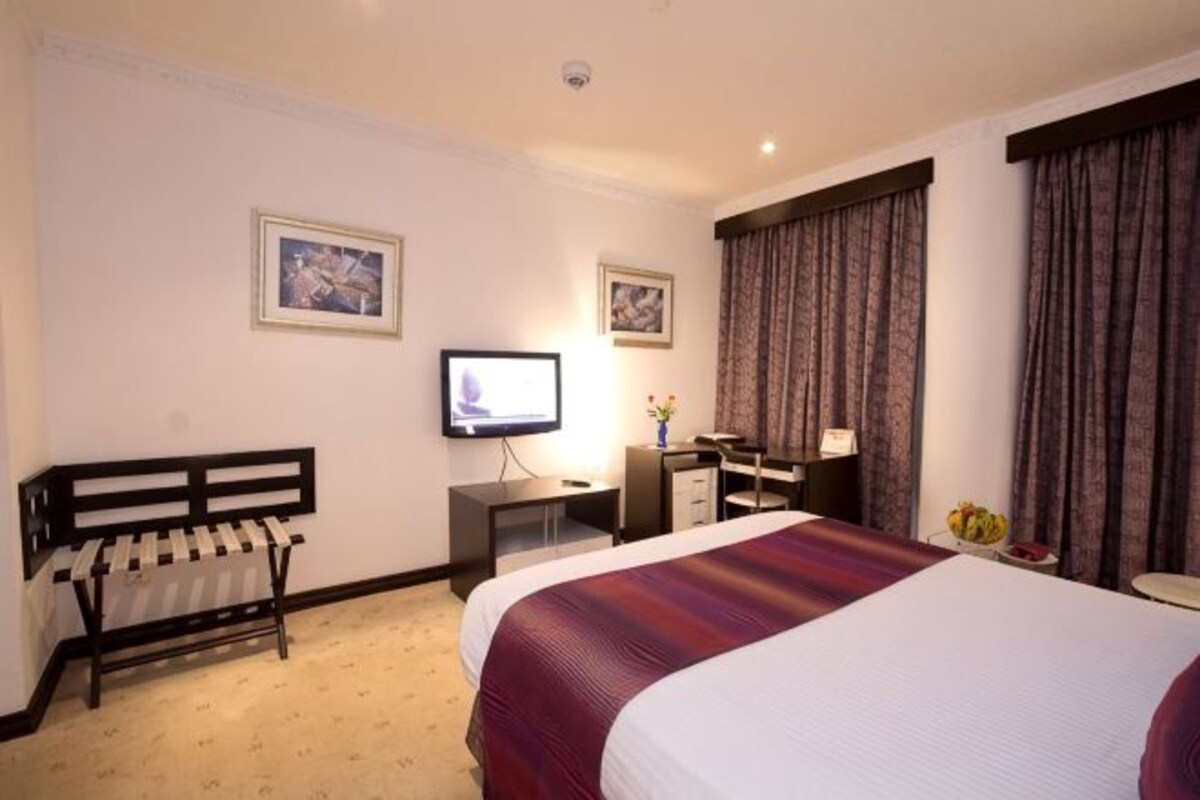 A hotel room with a bed, a desk, a chair, a television, and curtains.