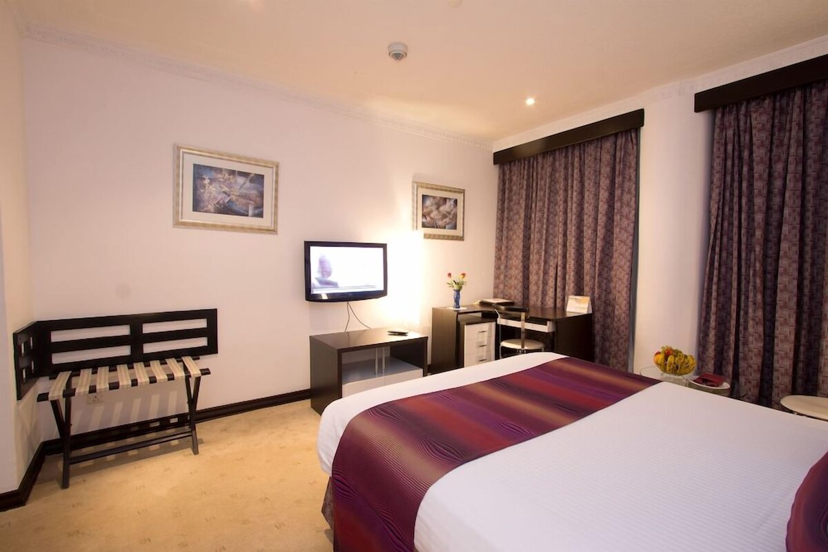 A hotel room with a large bed, a desk with a computer, a television, and two framed pictures on the wall.