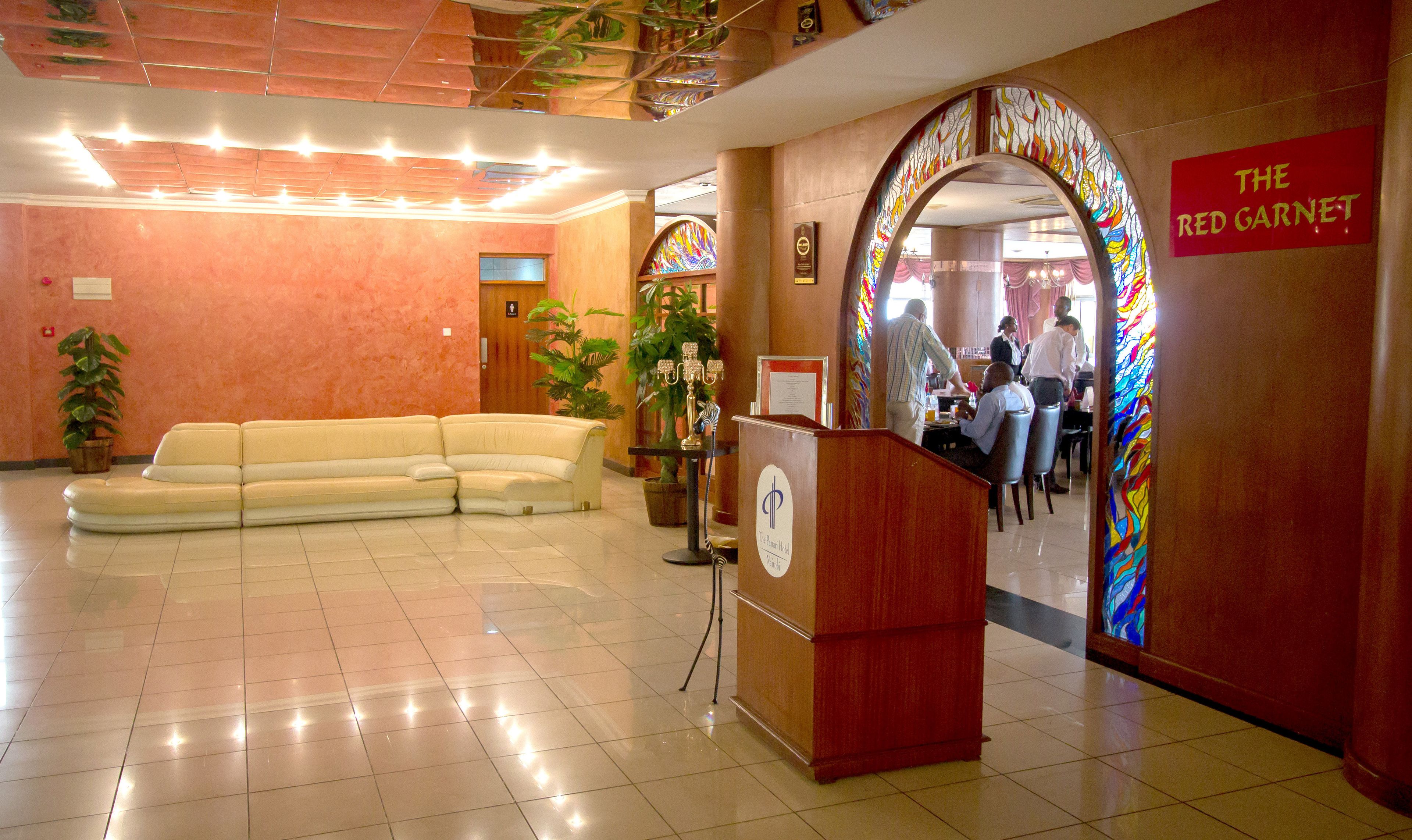 Un vestíbulo de hotel con mostrador de recepción, un sofá y un área de comedor visible a través de un arco.