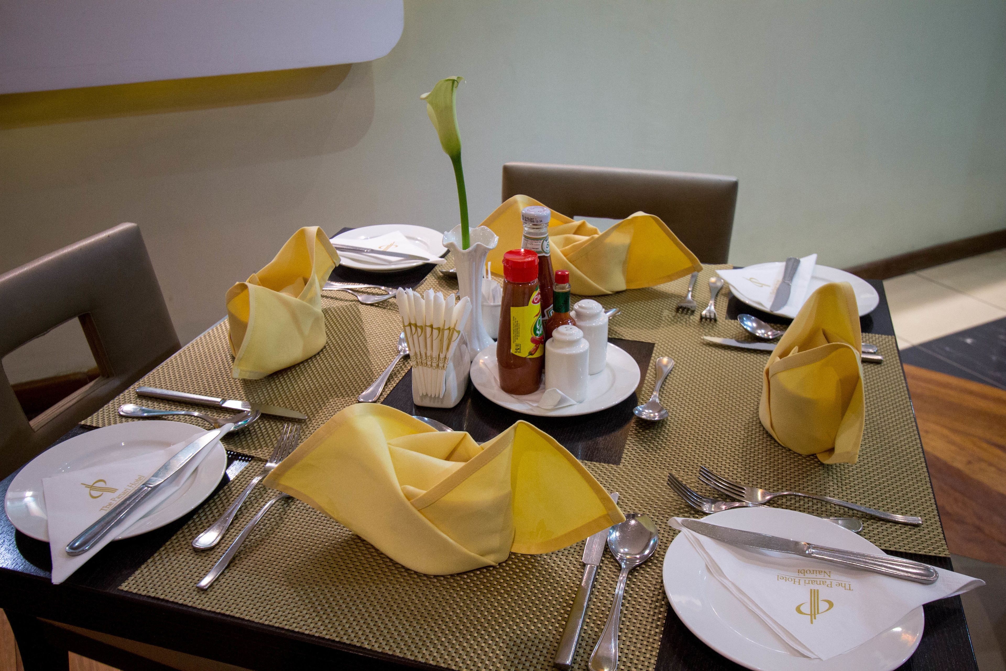 Une table à manger élégamment dressée, avec des serviettes jaunes, des couverts et des condiments.