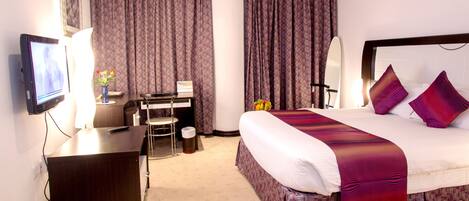 A hotel room with a bed, a desk, a chair, a TV, and curtains.