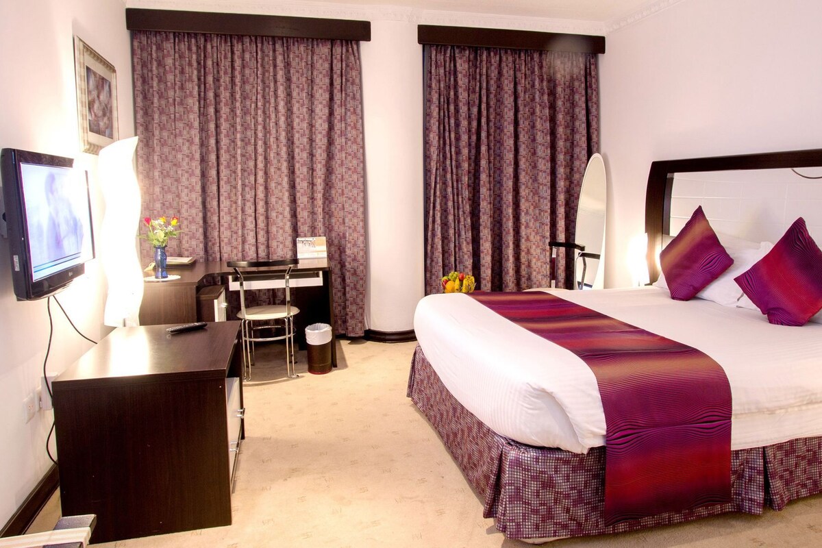 A hotel room with a bed, desk, chair, TV, and curtains.