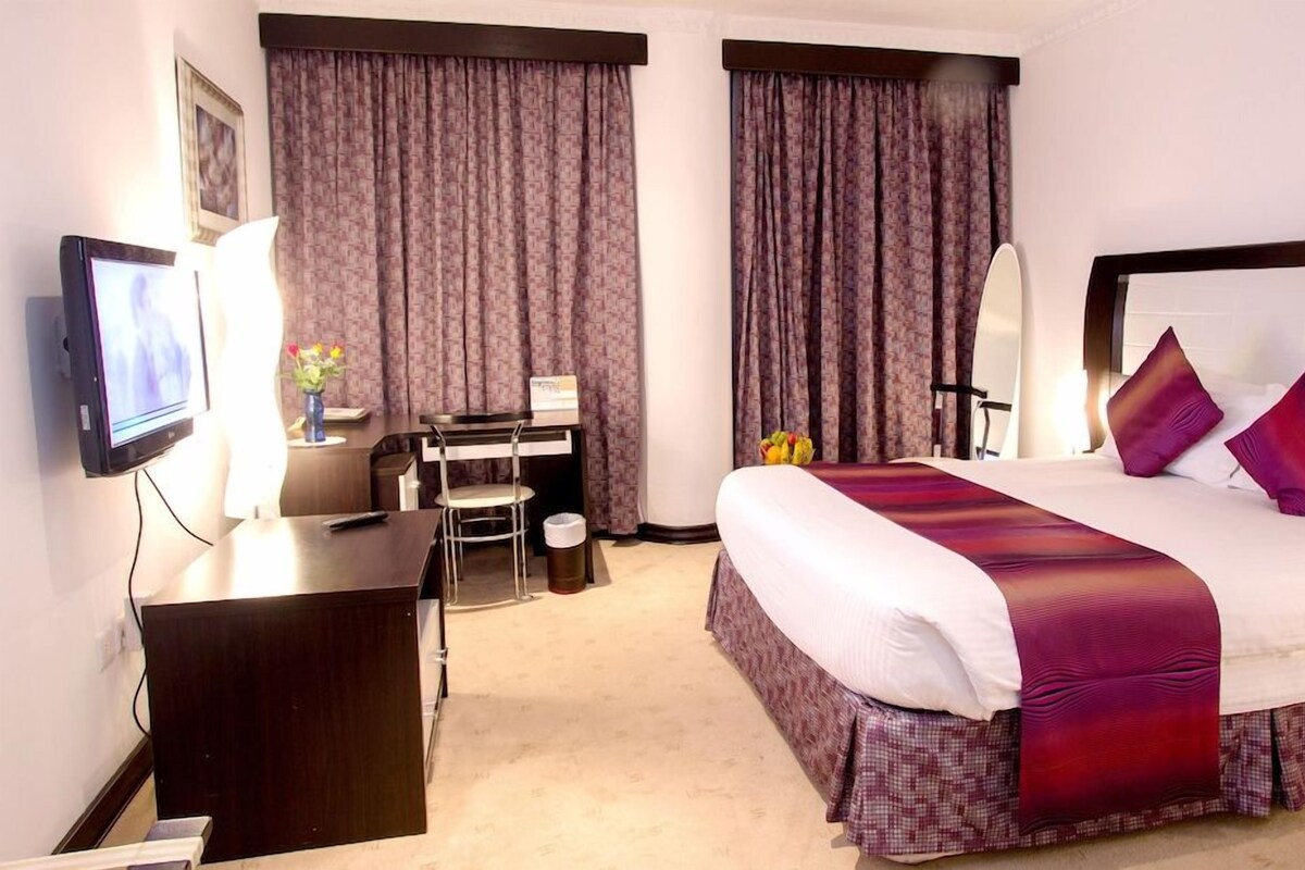 A hotel room with a bed, a desk, a chair, a television, and curtains.