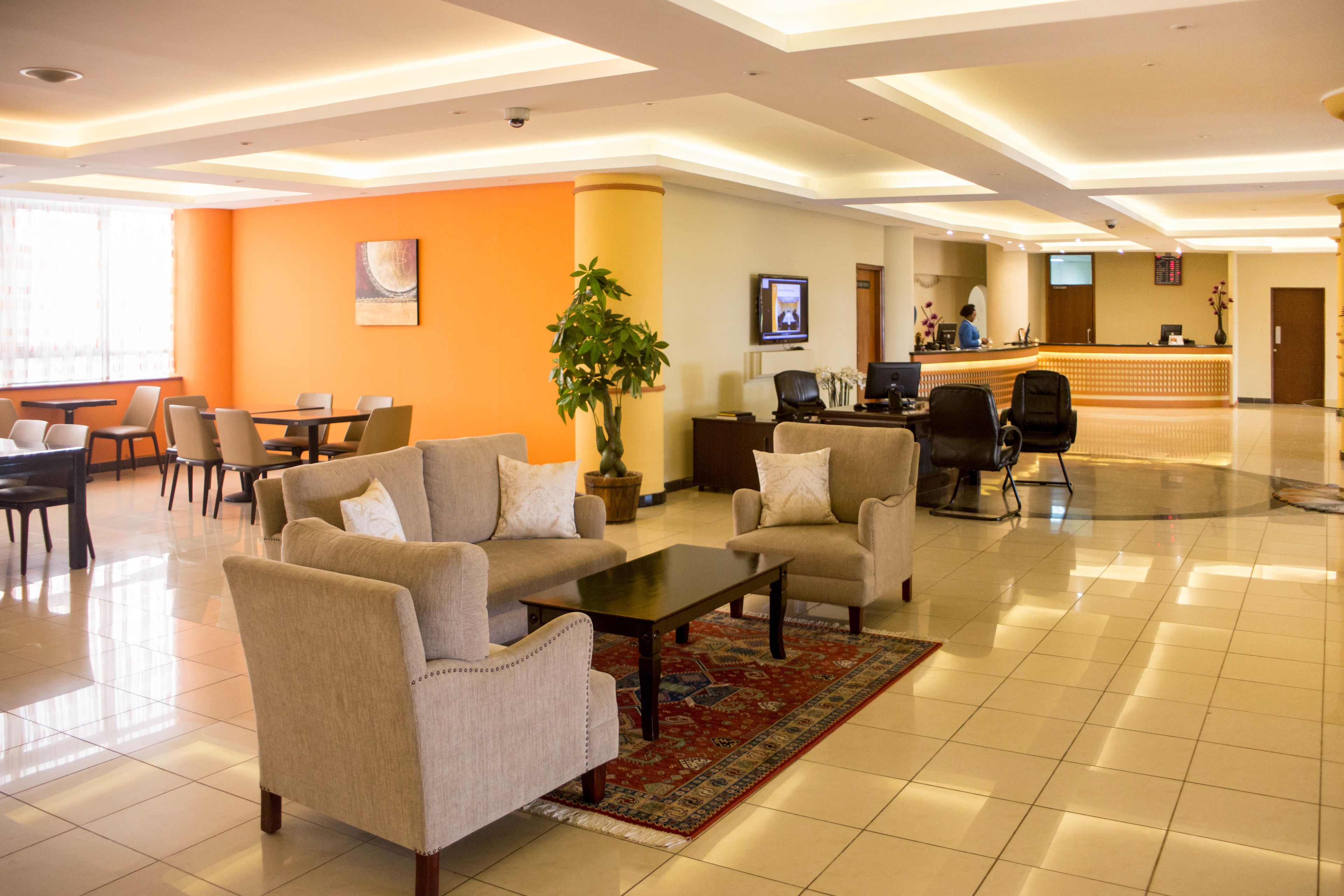 A hotel lobby with a reception desk, seating area with sofas and chairs, a large plant, and a tiled floor.