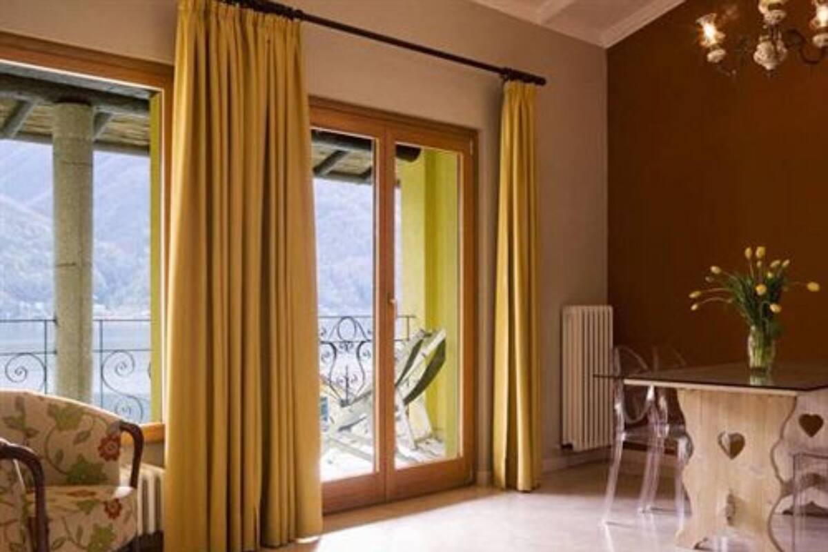 A room with a large window, yellow curtains, a chair, a table with a vase of flowers, and a radiator.