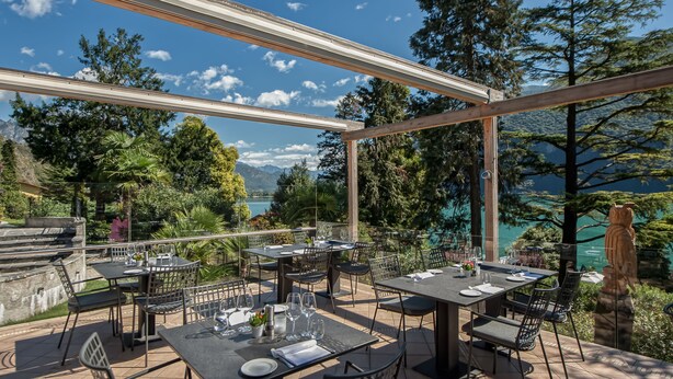 An outdoor dining area with tables and chairs, overlooking a mountainous landscape and a body of water. - Residenza Lago di Lugano (Porlezza)