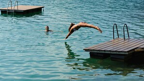 A person diving into a body of water from a wooden dock. - Residenza Lago di Lugano (Porlezza)