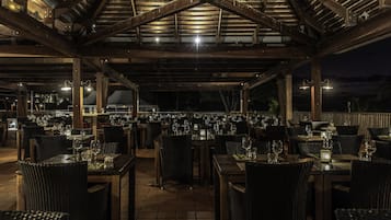 Un restaurant en plein air avec des poutres en bois et des tables dressées pour le dîner, offrant une vue sur le ciel nocturne.
