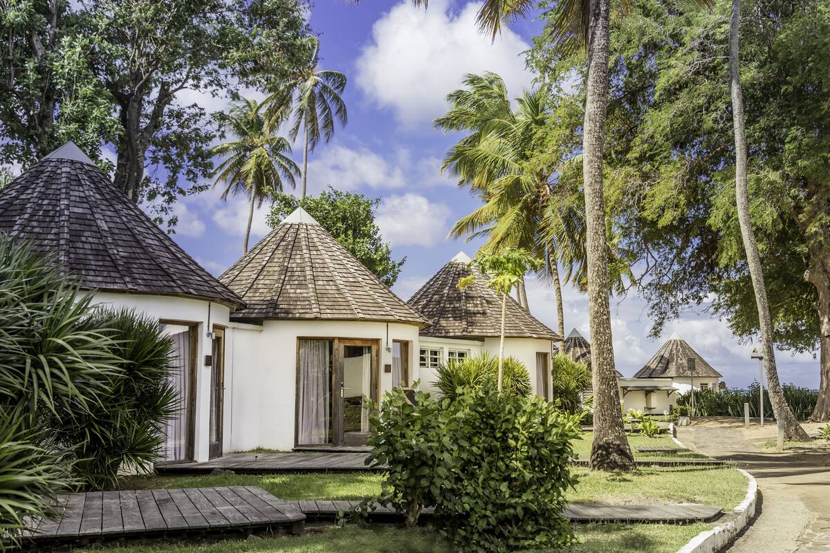 Eine Reihe von bungalows mit kegelförmigen Dächern, umgeben von üppiger Vegetation und Palmen.