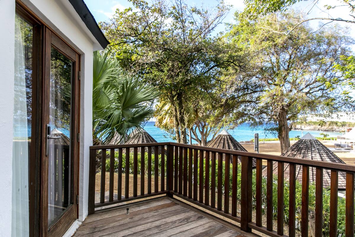 Eine Holzterrasse mit Geländer, mit Blick auf einen Strand und Palmen.