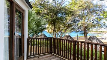 A wooden deck with a railing, overlooking a beach and palm trees.