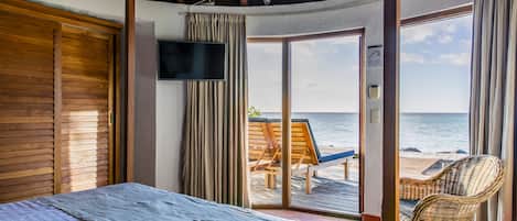 A bedroom with a bed, a TV, and a view of the beach.