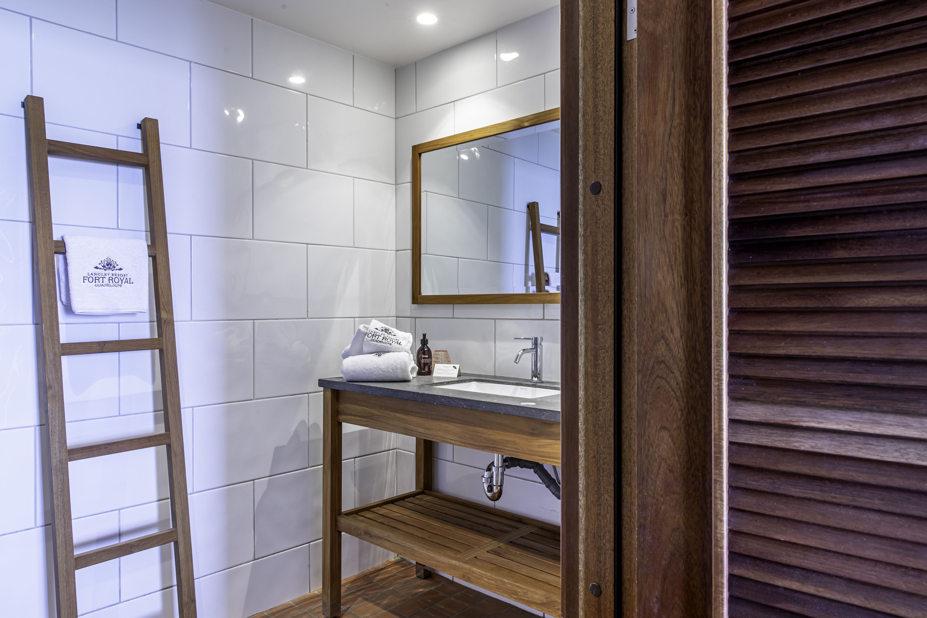 A bathroom with white tiles, a wooden vanity with a mirror, and a wooden ladder.