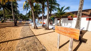 Un restaurante frente al mar con un letrero, palmeras y sombrillas de playa.