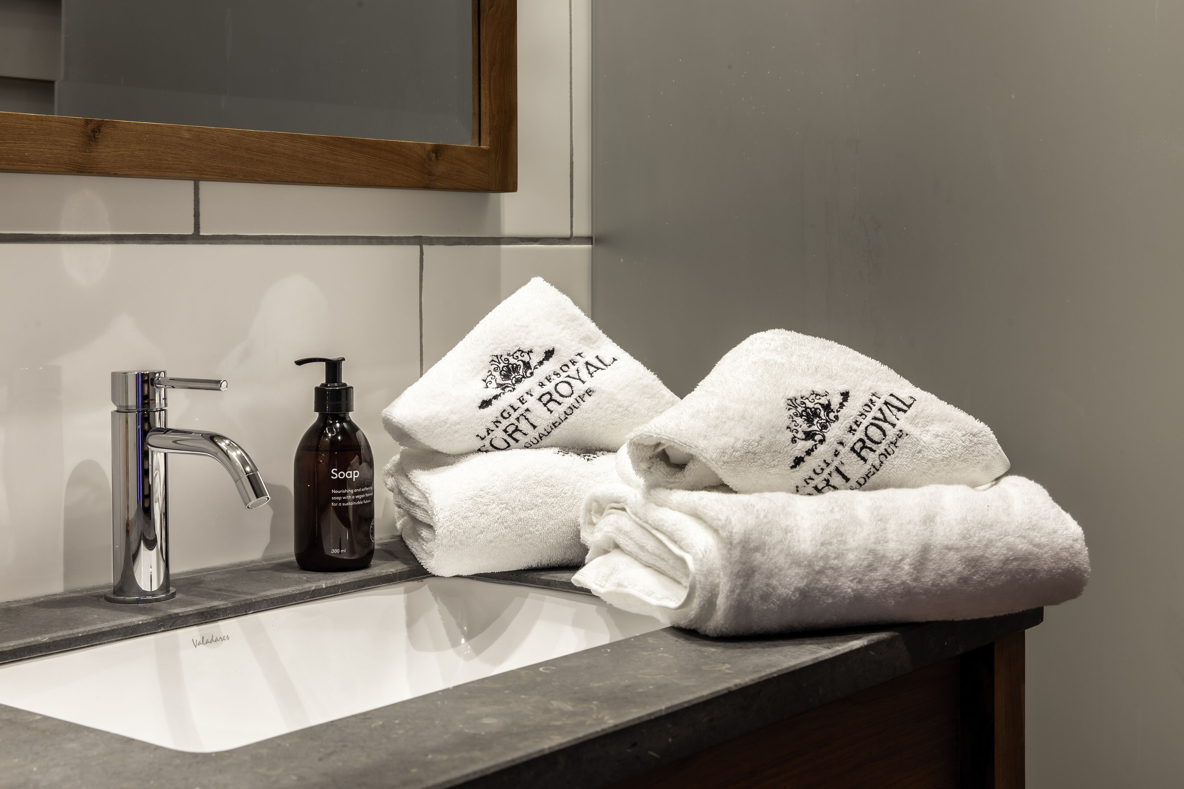 A bathroom with a sink, a soap dispenser, and three towels stacked on the counter.