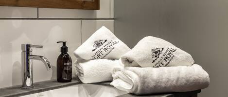 A bathroom with a sink, a soap dispenser, and three towels stacked on the counter.