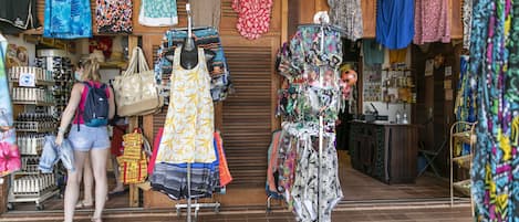 Una tienda de ropa con percheros llenos de vestidos y una exhibición de bolsos.