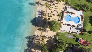 An aerial view of a resort with a swimming pool, beach, and palm trees. - Langley Resort Fort Royal (Deshaies)