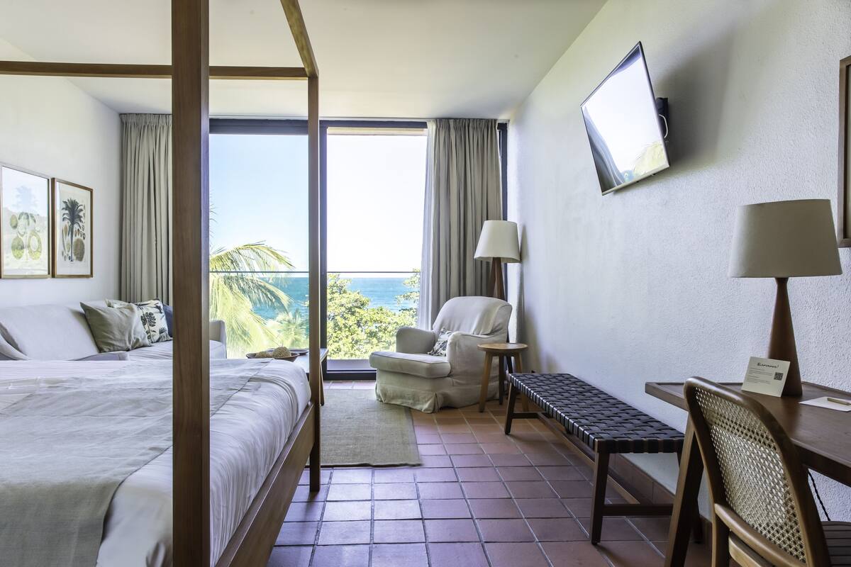Ein Hotelzimmer mit Bett, Sessel, Schreibtisch und Fernseher.