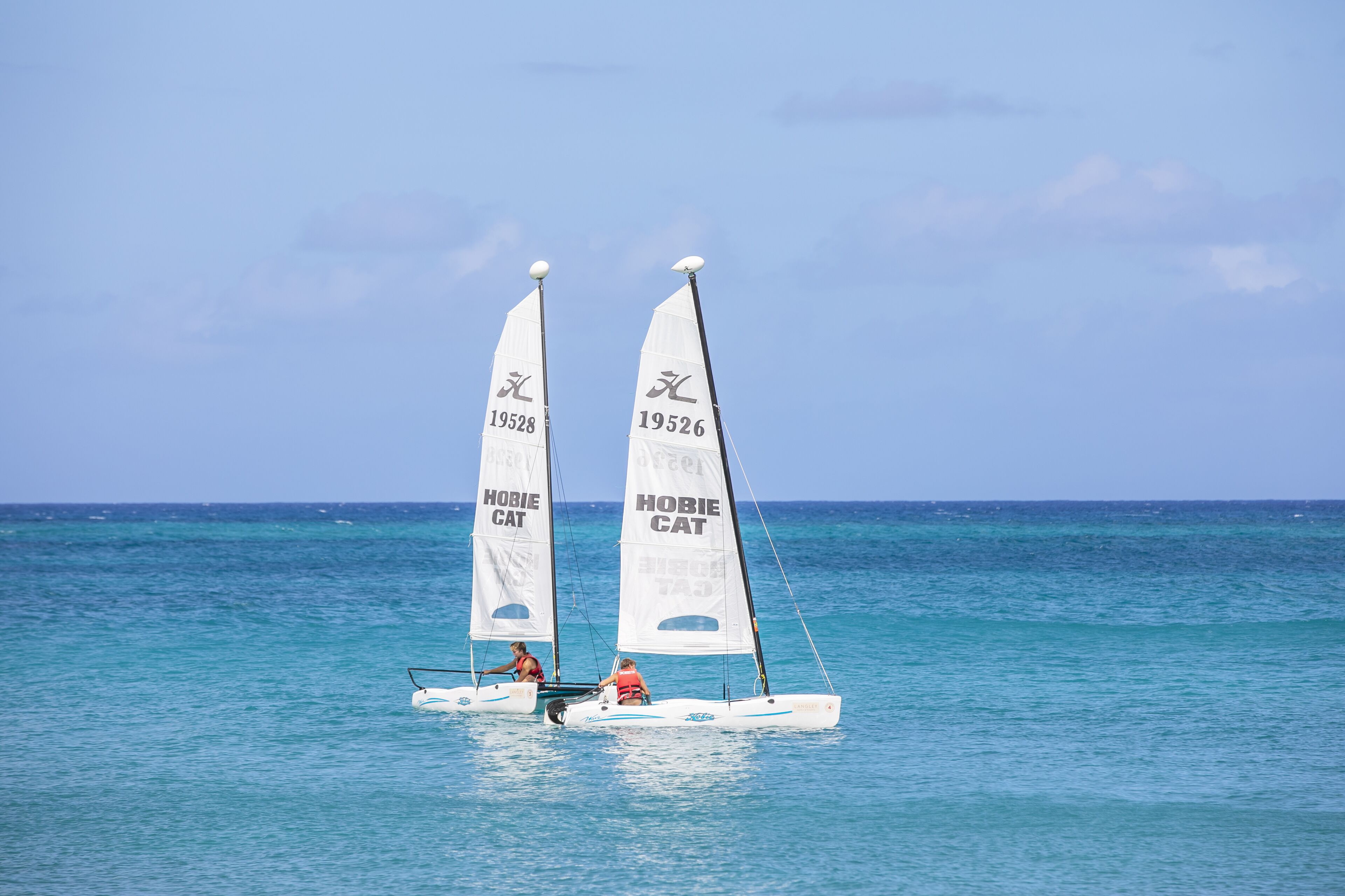 A sailboat with two sails labeled "Hobie Cat" on a calm sea.