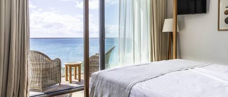 A hotel room with a bed, a TV, and a view of the ocean.