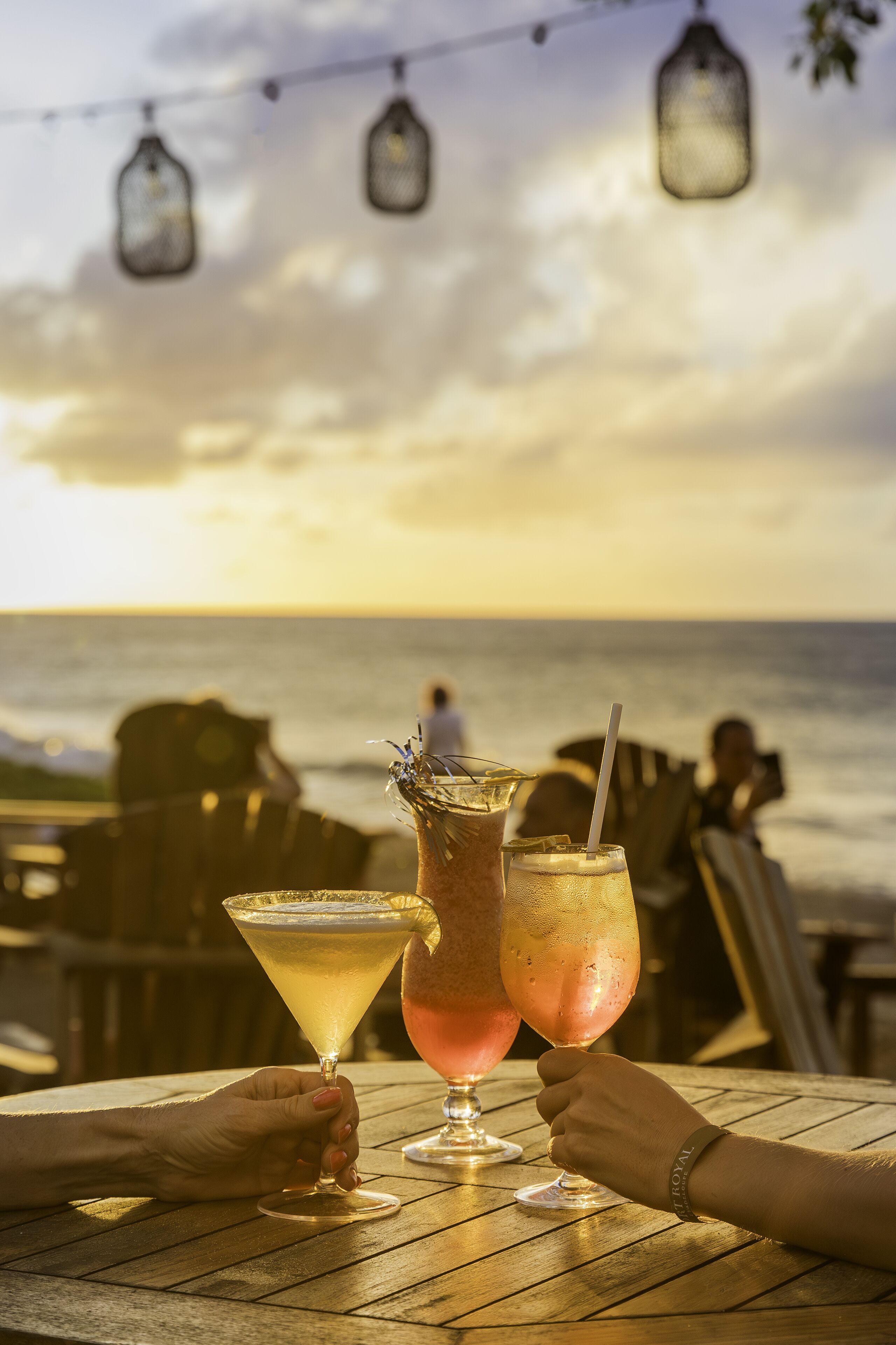 Una mesa de madera con dos bebidas, un atardecer al fondo y una persona a lo lejos.