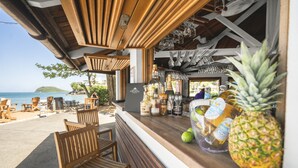 A beachside bar with wooden furniture, a pineapple, and various bottles. - Langley Resort Fort Royal (Deshaies)