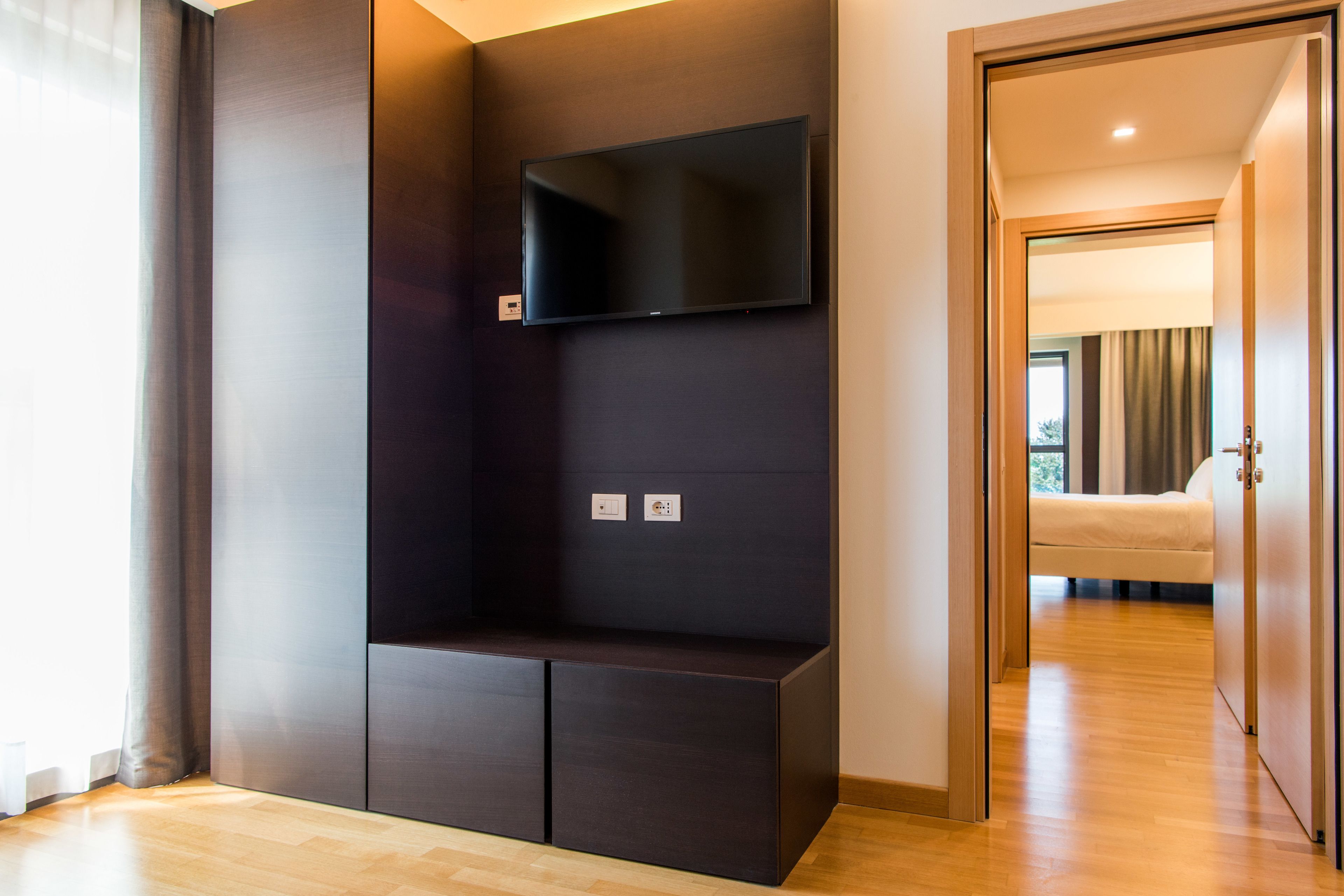 Ein modernes Zimmer mit integriertem Fernseher, Holzboden und einem Bett im Hintergrund.