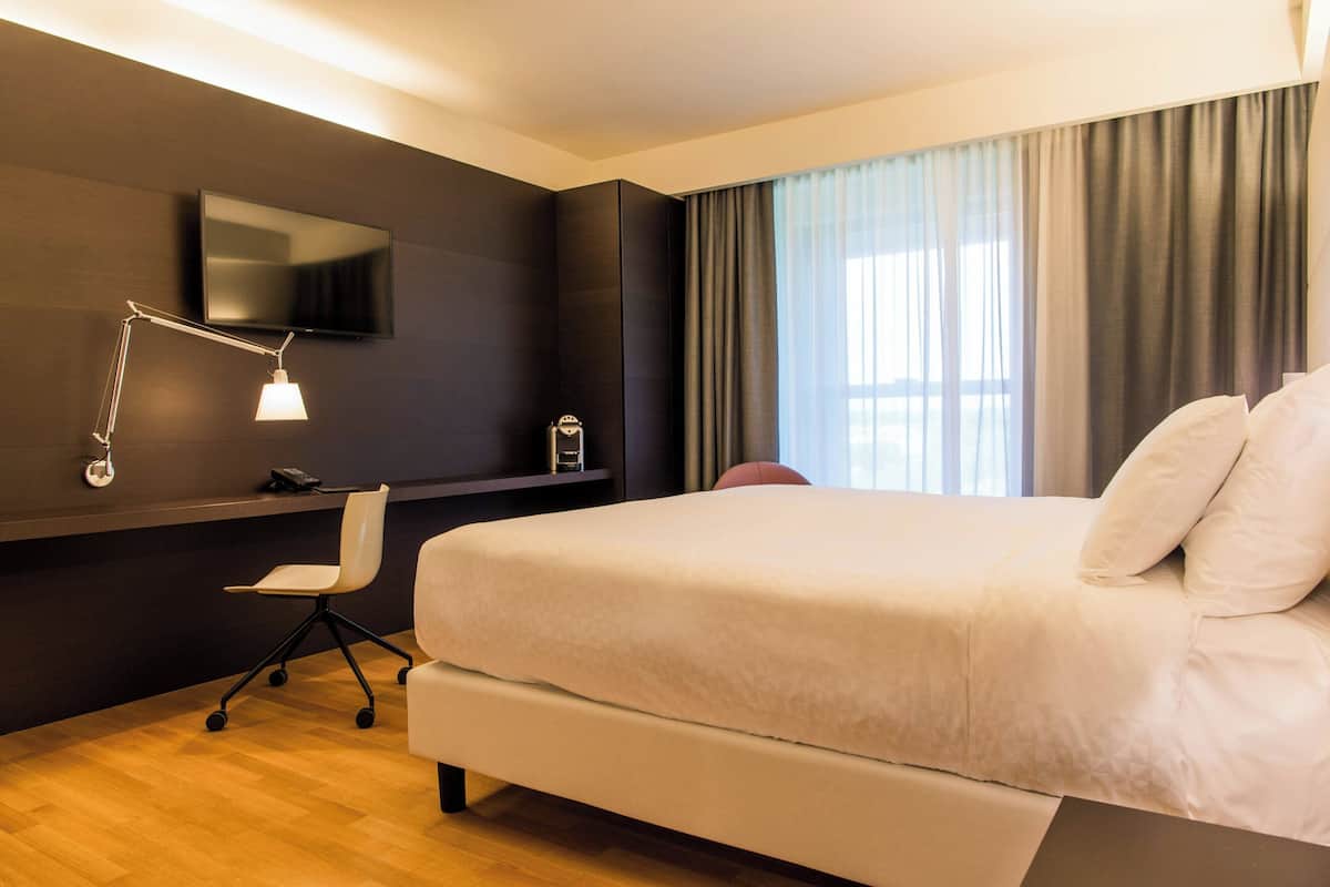 Een moderne hotelkamer met een groot bed, een bureau met stoel, een aan de muur bevestigde televisie en een raam met gordijnen.