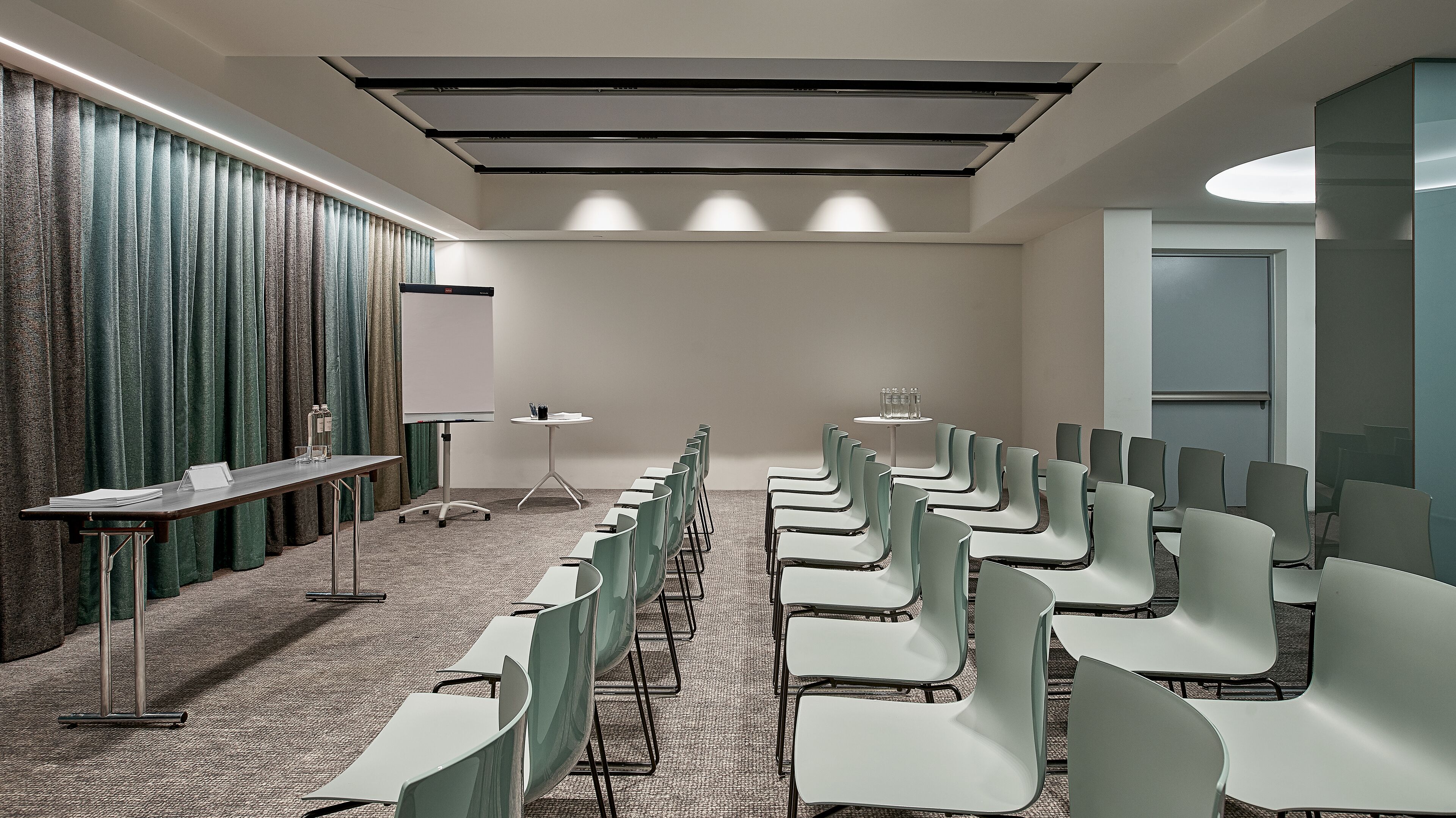 Ein Konferenzraum mit Reihen von Stühlen, einer Tafel und einem Tisch mit Wasserflaschen.