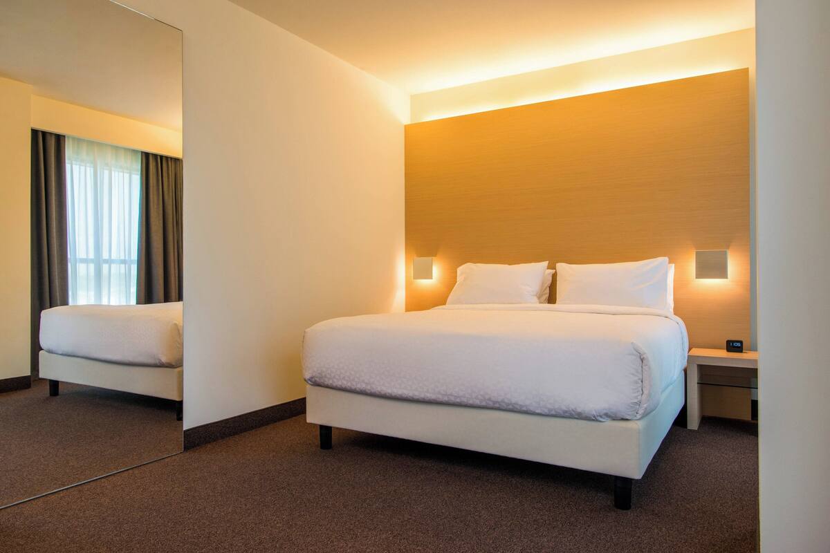Een hotelkamer met een groot bed, nachtkastjes, een spiegel en een raam met gordijnen.