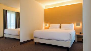 A hotel room with a large bed, bedside tables, a mirror, and a window with curtains.