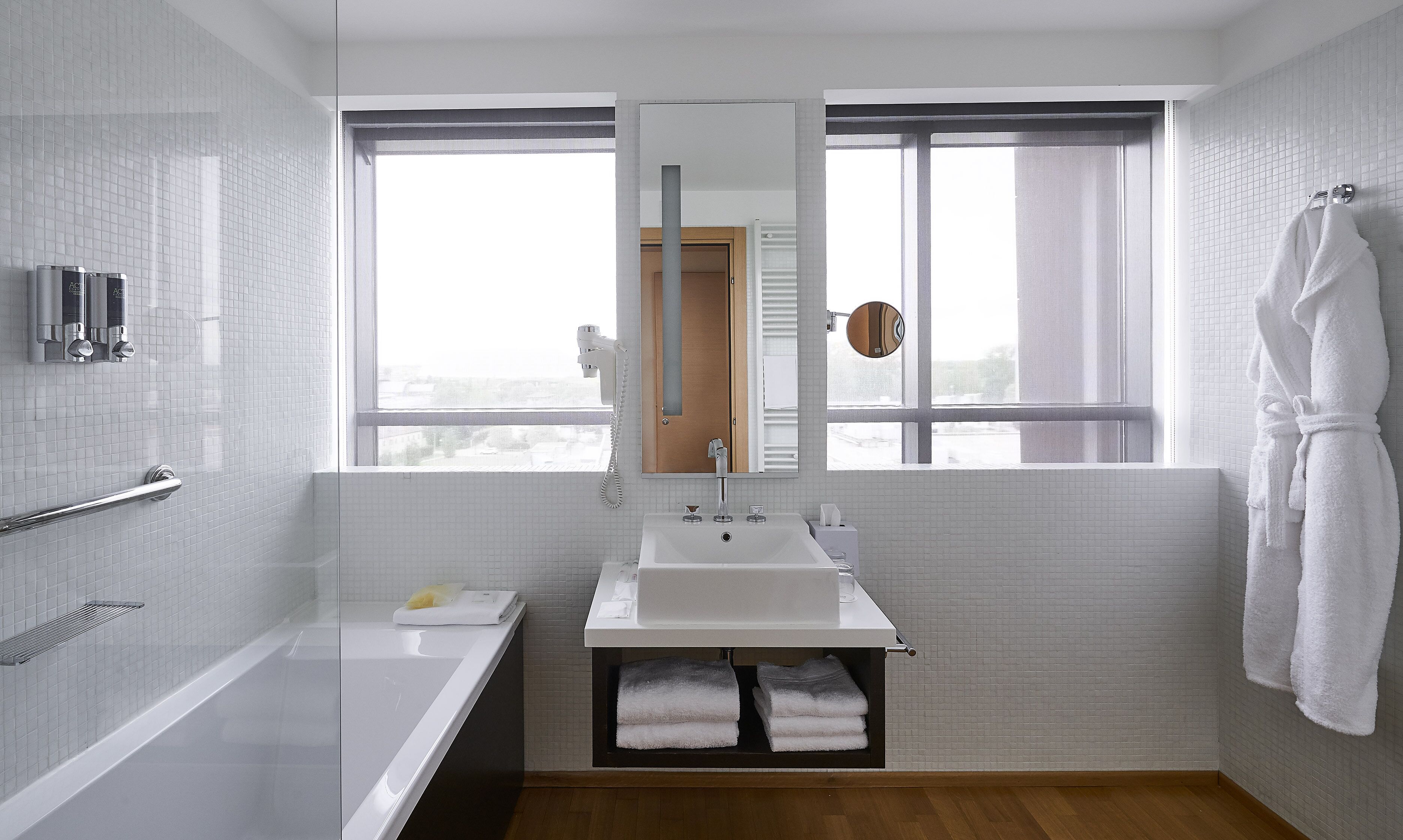 Un bagno moderno con una vasca, un lavandino e uno specchio. Si vede una finestra con vista all'esterno e un porta asciugamani con un asciugamano bianco.