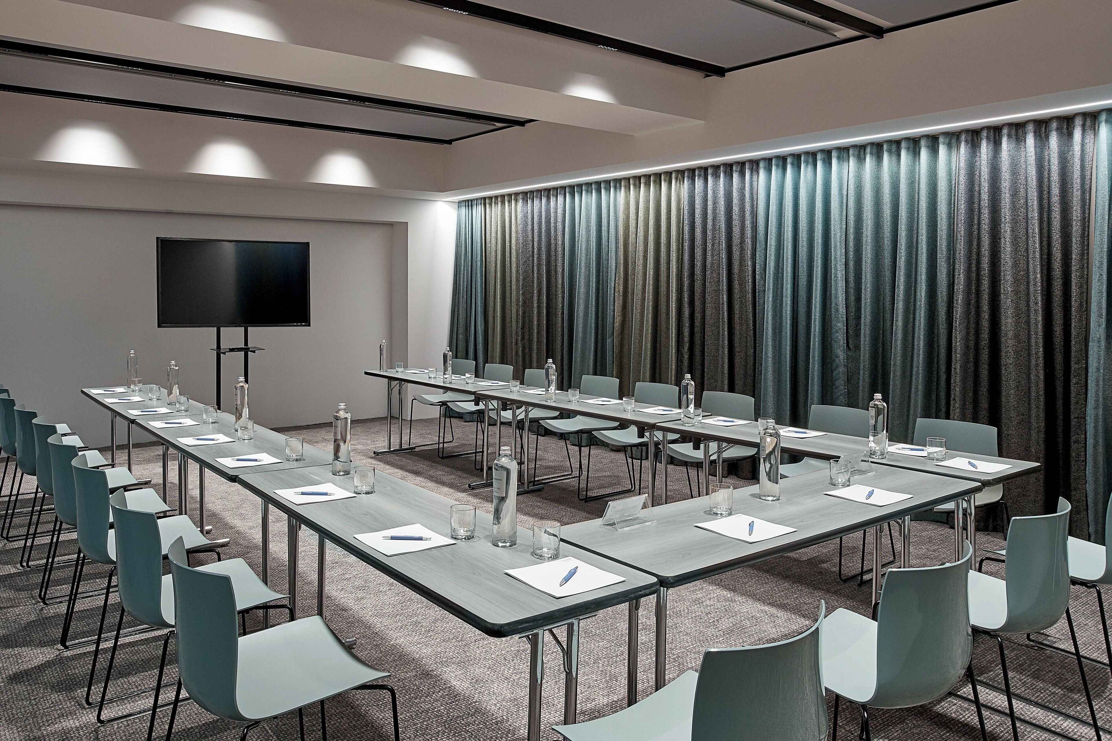 A conference room with a long table, chairs, a flat-screen TV, and a curtain backdrop.
