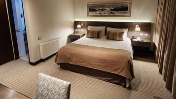 A hotel room with a large bed, bedside tables, a nightstand, a window with curtains, and a view of a snowy landscape.