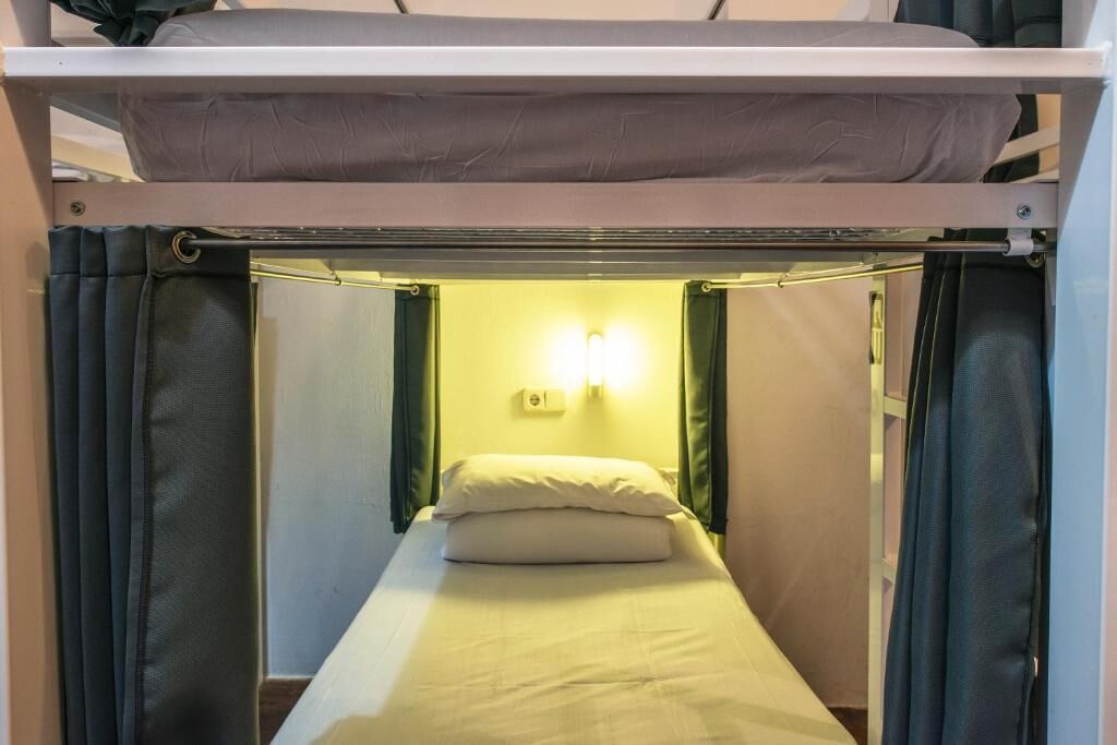 Una cama compacta con cabecera, cortinas y una lámpara fijada a la pared.
