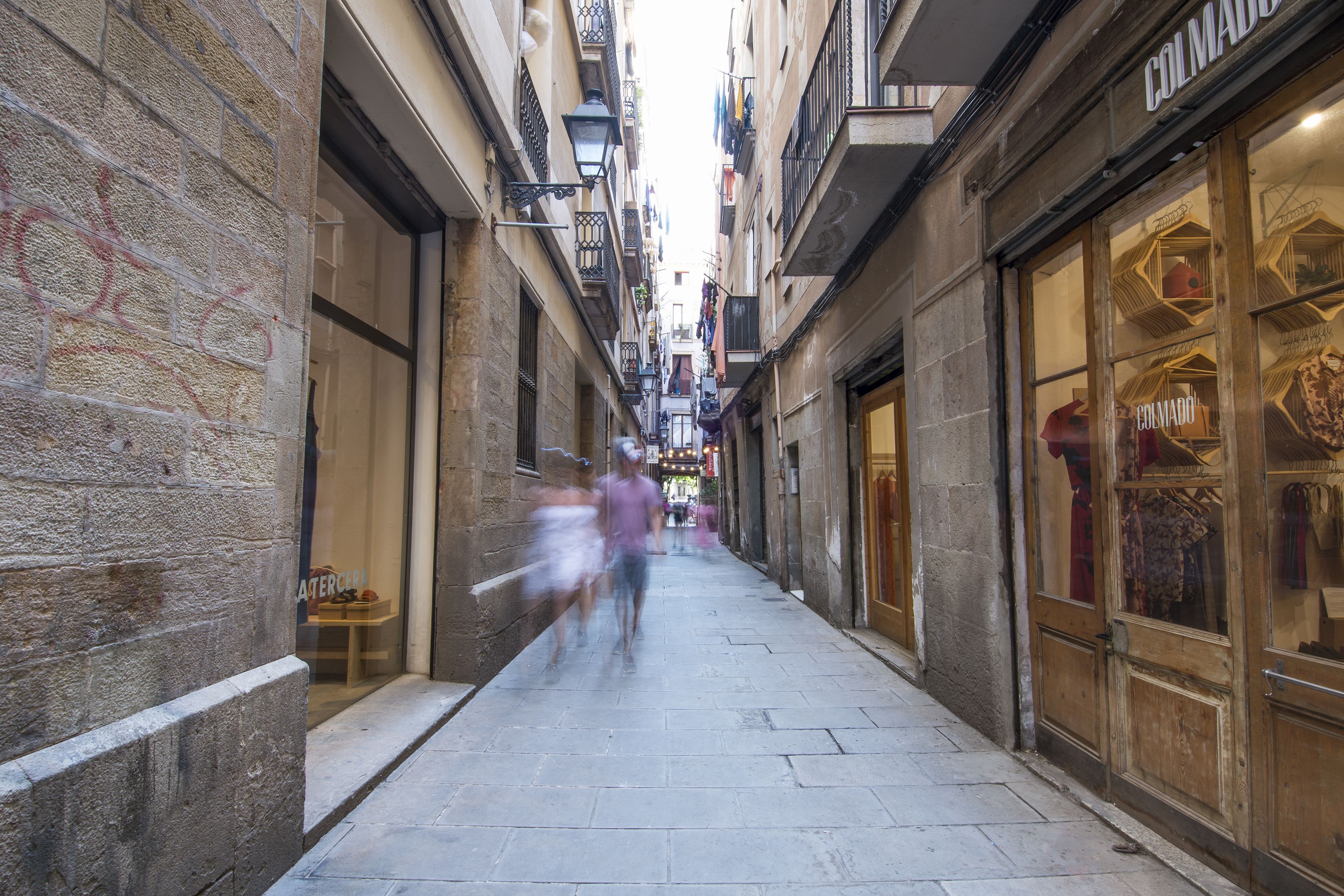 A narrow street with shops on either side, including a visible storefront with the name 'COLMADO'.